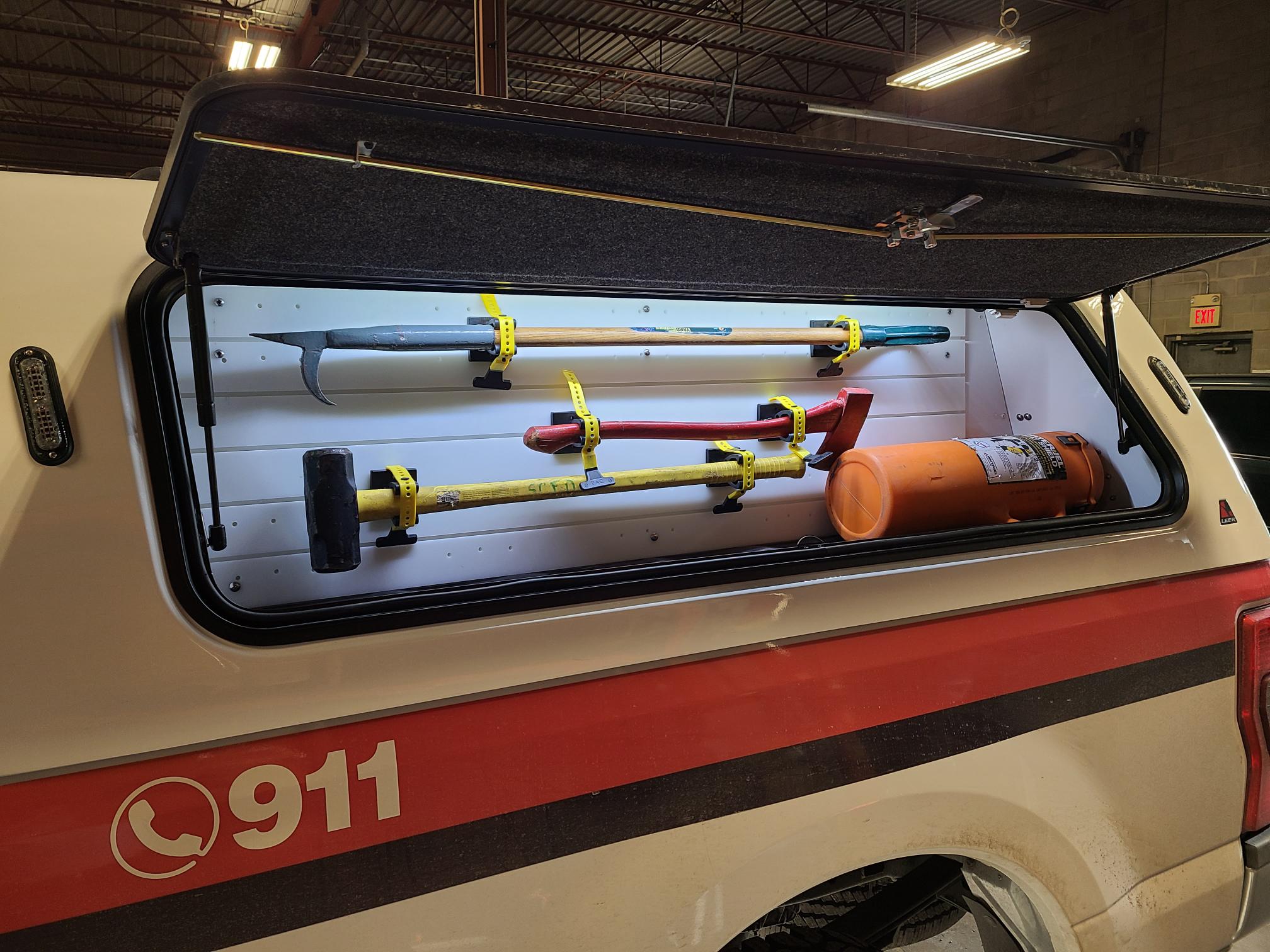 Illuminated emergency vehicle side compartment with organized firefighting hand tools